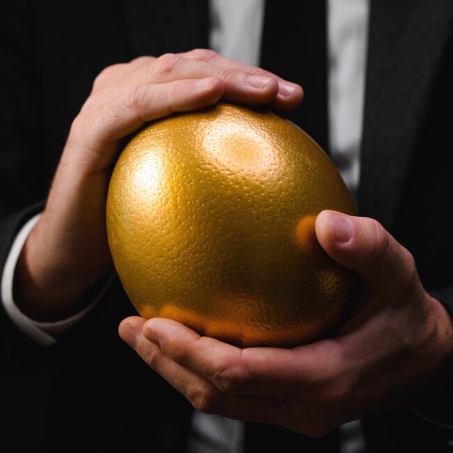 Golden egg in hands of elegant businessman as symbol of guaranteed success, profit or wealth.